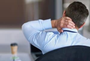 man-with-crick-in-neck-holding-back-of-neck-while-sitting-at-desk