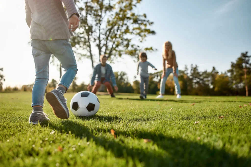 Family playing soccer in the park, sunny day.